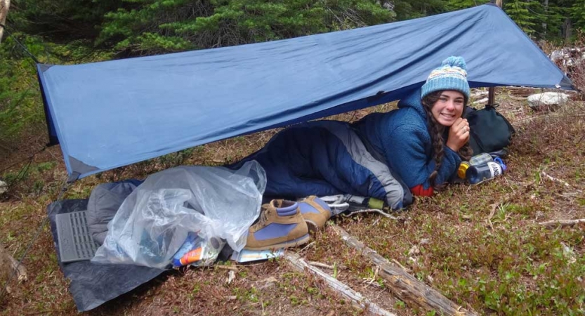 a person smiles while laying under a tarp shelter